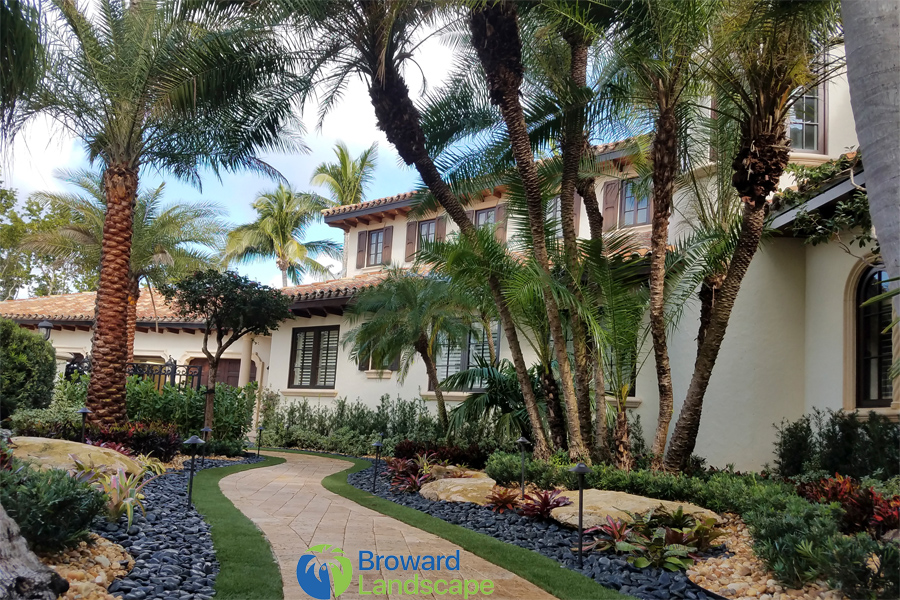 A tropical garden path leading to a white house with palm trees.