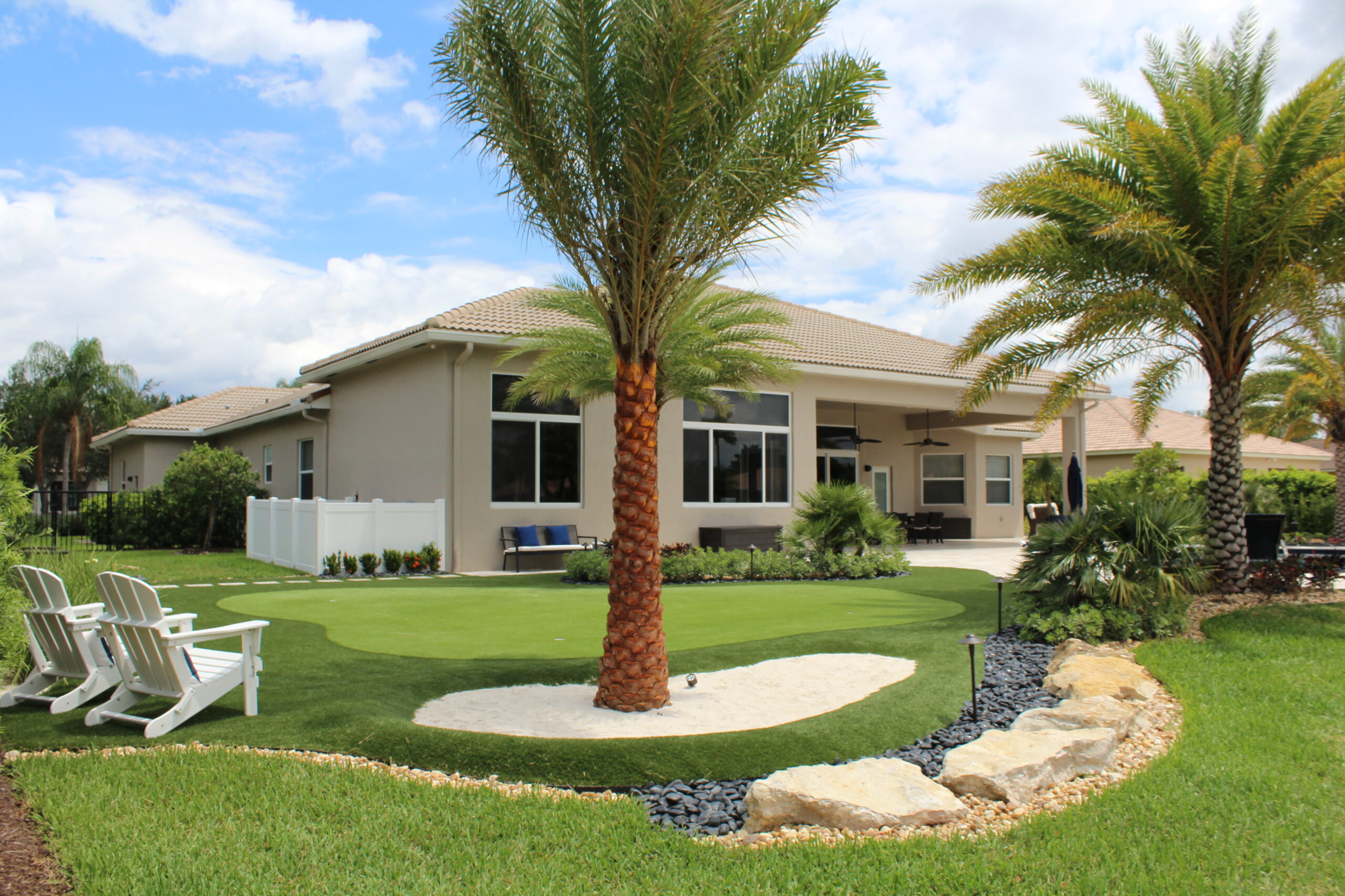 Modern white house with palm trees and a well-kept lawn under a blue sky.