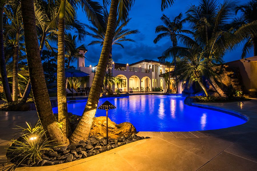 Luxurious villa with a glowing pool surrounded by palm trees at night.